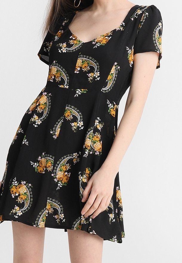 Svart kortärmad klänning med rundad halsringning, prydd med gula blommönster och intrikata gröna detaljer, tillverkad av lättviktsmaterial.