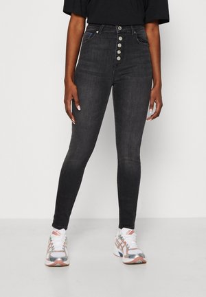 Person iført højtaljede sorte skinny jeans med fem knapper og hvide sneakers med pink og sølv detaljer.