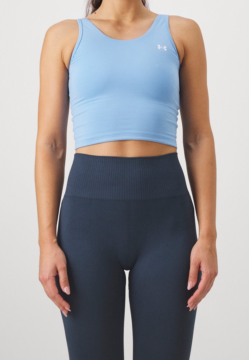 Femme portant un débardeur court bleu clair et un legging taille haute bleu foncé, debout devant un fond blanc uni.