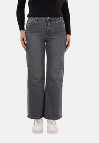 Jeans in denim scuro con vestibilità a gamba dritta, caratterizzati da una vita alta, cinque tasche e dettagli di cucitura. Abbinati a sneakers bianche.