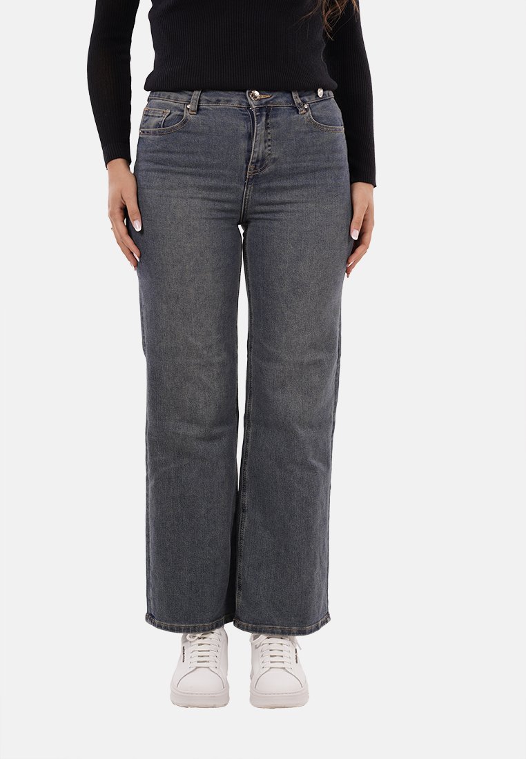 Jeans in denim scuro con vestibilità a gamba dritta, caratterizzati da una vita alta, cinque tasche e dettagli di cucitura. Abbinati a sneakers bianche.