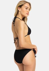 Svart bikini med en strukturerad rutnätsdesign, med justerbara knytband på toppen och sidorna av botten.