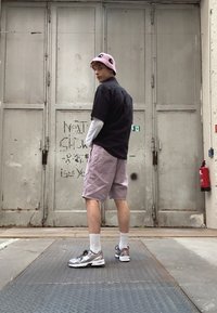 Svart kortermet skjorte, lys lilla shorts, rosa bøttehatt, hvit langermet skjorte under, joggesko med sølvdetaljer.