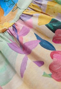 Tessuto floreale con texture morbida e leggera. Presenta fiori colorati in tonalità di rosa, giallo e viola su uno sfondo pallido.