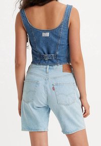 Denimskjorta med breda axelremmar och samlad detalj vid midjan, tillsammans med ljusblå denimshorts med bakfickor och ett varumärkesmärke.