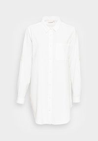 Camisa branca de botão de mangas longas, feita de um tecido texturizado. Apresenta um bolso no peito e botões dourados por toda a frente e nas mangas.