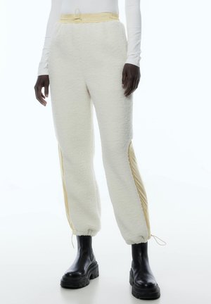 Cremefarbene Fleece-Sweatpants mit gelben Seitenpanelen; elastischer Bund und Bündchen; verfügt über einen Kordelzug für eine verstellbare Passform.