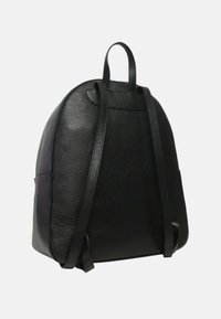 Czarny skórzany plecak o zaokrąglonym kształcie, gładkiej fakturze, z dwiema długimi ramiączkami i uchwytem na górze. Podkreślony minimalistycznymi elementami designu.