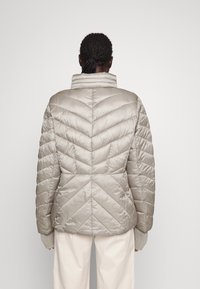 Jasno beżowa kurtka puchowa z wysokim kołnierzem, wzorem w zygzak oraz dzianinowymi mankietami. Gładka, błyszcząca faktura.