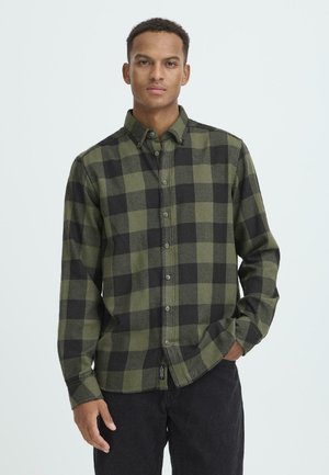 Chemise à carreaux verte et noire, fabriquée en tissu doux. Dotée d'un col, de boutons sur le devant et de manches longues. Assortie avec un pantalon noir.