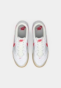 Balti sportiniai bateliai su raudonais akcentais, kvėpuojanti medžiaga, paminkštintas apykaklė ir guminis padas. Su raišteliais ir ryškia Nike prekių ženklą.
