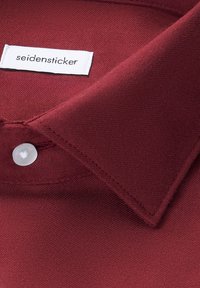 Bordeauxhemdkraag met een zachte textuur, een witte knop en een ingestikte label met de tekst "seidensticker" in een contrasterend lettertype.