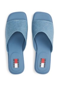 Sandales glissantes bleues avec un dessus en denim texturé, design à sangle croisée arrondie et semelle en caoutchouc. Présente une étiquette de logo en rouge, blanc et bleu.