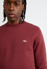 Maroon sweatshirt van katoenmix, met een ronde hals, geribbelde manchetten en een opvallende rechthoekige Dickies-patch op de borst.