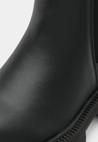 Detailný záber na hladkú čiernu koženú členkovú obuv s viditeľným šitím a textúrovaným okrajom podrážky.