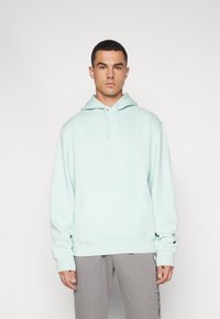 Felpa leggera blu con cappuccio regolabile, tasca a marsupio, polsini a costine e un piccolo logo sul lato sinistro del petto. Abbinata a pantaloni della tuta grigi.