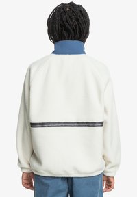 Weißer Fleece-Pullover mit blauem Kragen, der ein flaches Band mit geometrischem Muster über den Rücken und gerippte Bündchen aufweist.