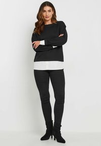 Musta pitkähihaine paita valkoisen paidan päällä, yhdistettynä mustiin tiukkoihin farkkuihin ja mustiin korkea nilkkabootseihin. Sileä kangas ja istuva muotoilu.