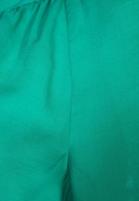 Zelená látka s měkkou texturou, s hladkým povrchem a mírným leskem, složená s viditelným švem podél švu.