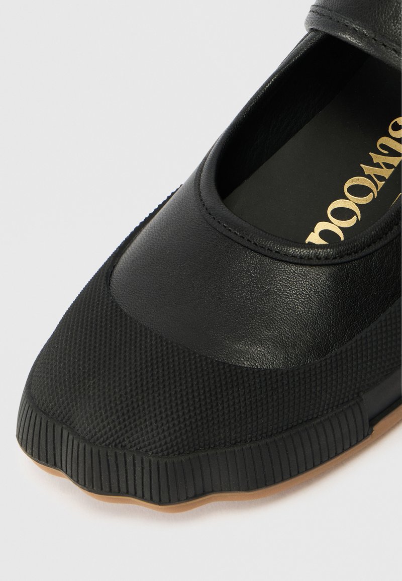 Scarpa nera con punta e suola in gomma testurizzata, tomaia in pelle liscia e testo dorato visibile sulla soletta.