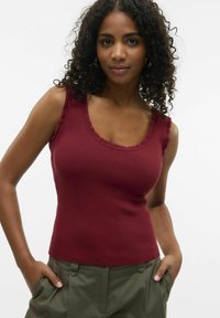 Top de tirantes burdeos acanalado con un escote en forma de picos y tirantes anchos, combinado con pantalones de cintura alta en tono verde oliva. Textura suave visible.