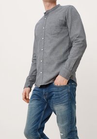 Grijs overhemd met knopen en een afgeronde kraag, voorzien van een borstzakje en een gestructureerde stof. Gecombineerd met blauwe, verweerde jeans.