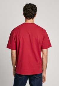 Czerwona bawełniana koszulka T-shirt z krótkim rękawem, okrągłym dekoltem i prostym dołem. Tył jest gładki, bez widocznych logo lub wzorów.