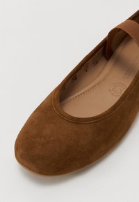 Brune semsket flatt sko med avrundet tå, elastisk stropp over toppen og myk innside. Har en glatt såle og minimal søm.