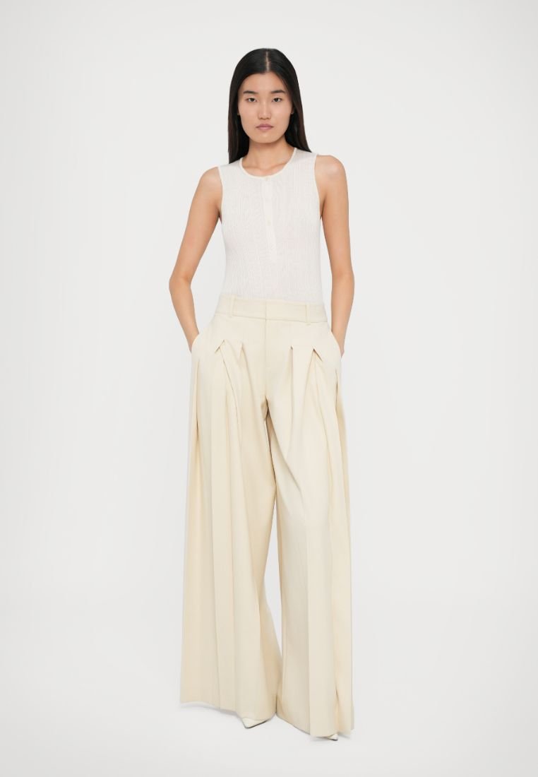 Pantalons larges beige clair avec des plis et des poches latérales, associés à un débardeur ajusté blanc cassé à côtes avec un détail de bouton.