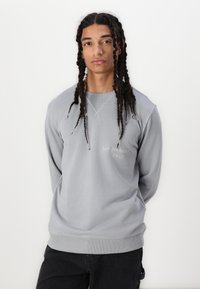 Grauer Pullover mit Rundhalsausschnitt, gerippten Bündchen und Saum. Verfügt über dezenten, in heller Stickerei gehaltenen Text "SAN BERNARDINO CALIF.".