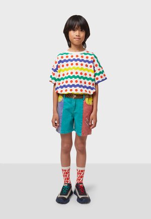 T-shirt multicolore con motivo a righe e pois, pantaloni corti in denim con design a patchwork, calze brillanti e scarpe sportive con accenti multicolori.