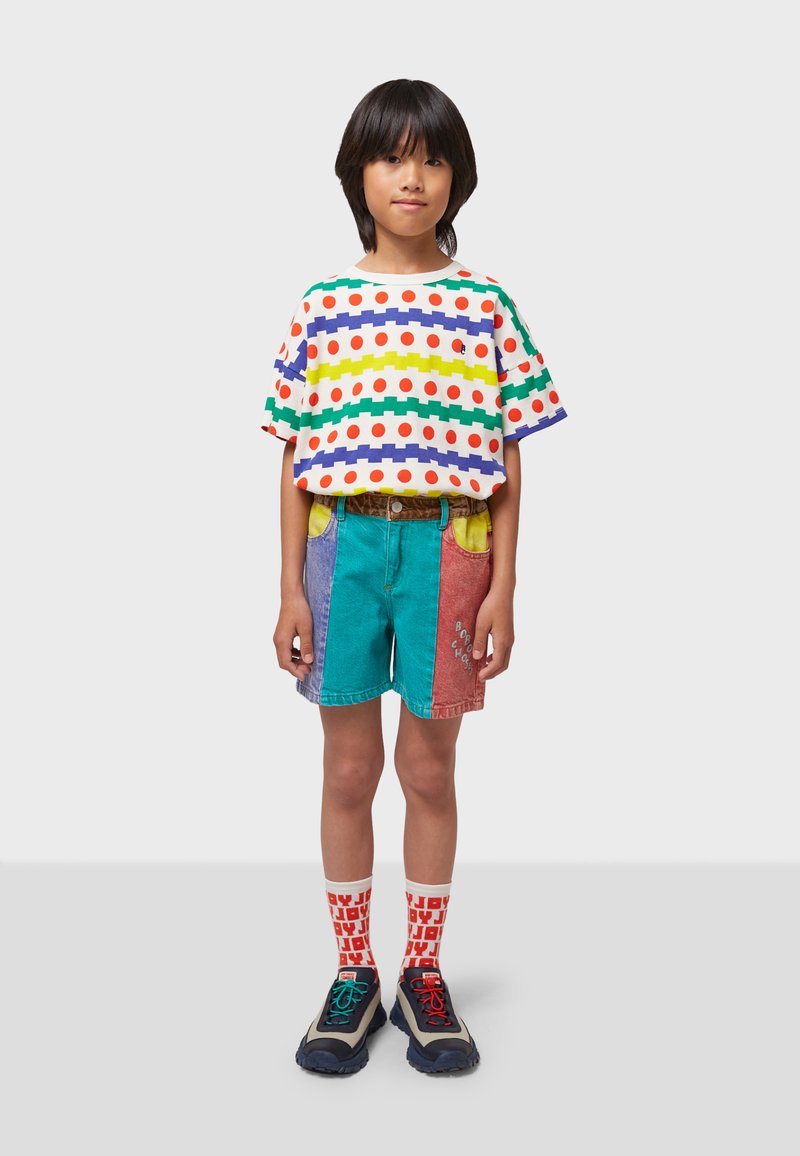 T-shirt à motifs multicolores avec rayures et pois, shorts en denim avec un design en patchwork, chaussettes vives et chaussures de sport avec des accents multicolores.