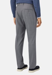 Sive prilagojene hlače z gladko teksturo, z enim zadnjim žepom in diskretnim vzorcem tkanine, v kombinaciji s temnimi čevlji.