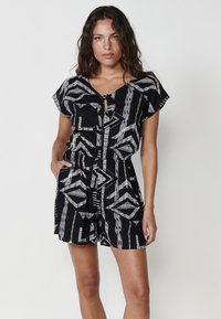 Zwarte playsuit met een geometrisch wit patroon, korte mouwen, een strikdetail bij de halslijn en zijzakken.