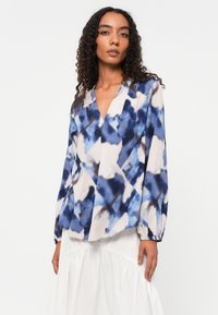 Seidenbluse mit blau-beigem abstraktem Muster, tiefem V-Ausschnitt und langen Ärmeln mit elastischen Bündchen. Leicht und fließendes Design.