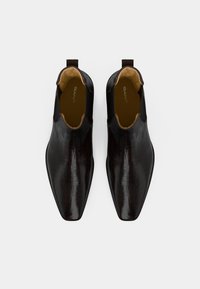 Botas de couro pretas com textura de crocodilo, bico pontudo e painéis laterais elásticos. O interior apresenta um forro bege. Logotipo da GANT visível.