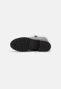 Black rubber boot sole with deep treads for grip. Features a smooth upper with a slight sheen and a small branded accent near the ankle.