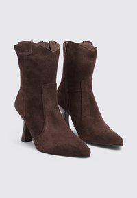 Bottes de cheville en daim marron avec un bout pointu et un talon bloc de hauteur intermédiaire. Dispose d'une fermeture à glissière latérale et de panneaux en tissu contrastants.