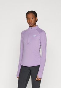 Ανοιχτό μοβ πουλόβερ με φερμουάρ στο πάνω μέρος και μήκος μέχρι το μισό στέρνο, κατασκευασμένο από απαλό ύφασμα, με κυρτή κάτω ραφή και ανοίγματα για τους αντίχειρες. Μικρό λογότυπο στο στήθος. Εφαρμοστή γραμμή.