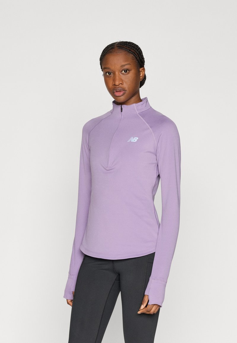 Ανοιχτό μοβ πουλόβερ με φερμουάρ στο πάνω μέρος και μήκος μέχρι το μισό στέρνο, κατασκευασμένο από απαλό ύφασμα, με κυρτή κάτω ραφή και ανοίγματα για τους αντίχειρες. Μικρό λογότυπο στο στήθος. Εφαρμοστή γραμμή.