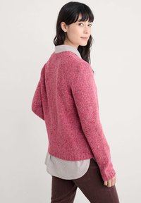Pulover roz pufoș cu un tiv striat și mâneci lungi, suprapus peste o cămașă cu guler stripedă albă și albastră, având o croială lejeră.