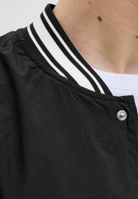 Veste bomber noire avec un col côtelé noir et blanc rayé. Comprend un détail de bouton-pression argenté et un tissu lisse et texturé.