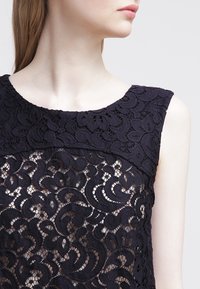 Black lace top featuring a floral pattern, a scoop neckline, and opaque lining. The texture is intricate and layered, with a fitted design.