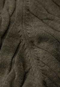 Pletená látka v tmavě olivově zelené barvě s texturovanými kabelovými vzory a hladkým povrchem. Měkký materiál se dobře splétá s viditelnými detaily švů.