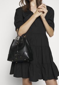 Bolso de mano negro de cuero con un acabado texturizado, base redonda y detalles en hardware dorado. El bolso cuenta con un cierre de cordón y un asa resistente.
