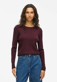 Burgundowy sweter w prążki z długimi rękawami, okrągłym dekoltem i miękką teksturą. Połączony z niebieskimi dżinsami o wysokim stanie. Prosty design.