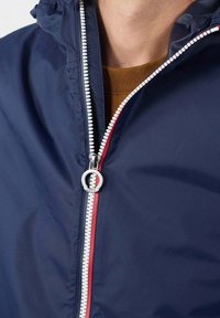 Marineblauer Windbreaker mit Reißverschluss, der rote und weiße Akzente aufweist. Glatte Textur und verstellbare Kapuze, mit einem minimalistischen Design.