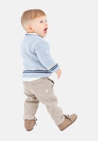 Suéter de punto azul claro con rayas marino y beige, pantalones de pana beige con bolsillos laterales y zapatos de ante marrones. El niño está girando.