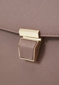 Sac à main texturé marron avec un fermoir doré et un détail de sangle rectangulaire, présentant une surface lisse et des motifs subtils.