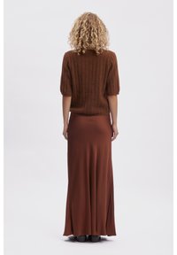 Un pull court à manches courtes en tricot à côtes marron, associé à une longue jupe fluide en satin marron, tombant élégamment jusqu'au sol.